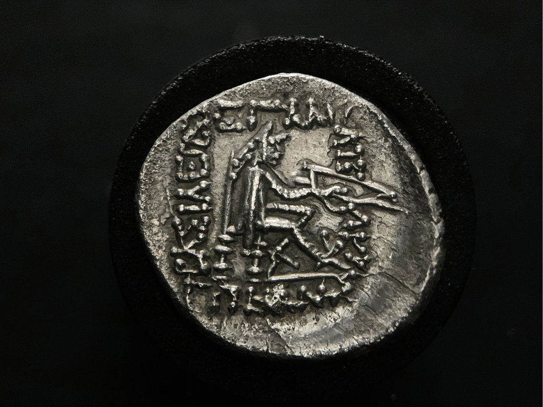 Archer seated right holding bow, Greek script surrounding